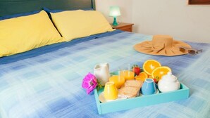 A neatly made bed with blue and yellow bedding, a tray of breakfast items including orange juice, a hat, and a pitcher of water. - Apollo's Terraces Beach apartments less than 20 m from the sea!Sirocco (Marinella di Selinunte)