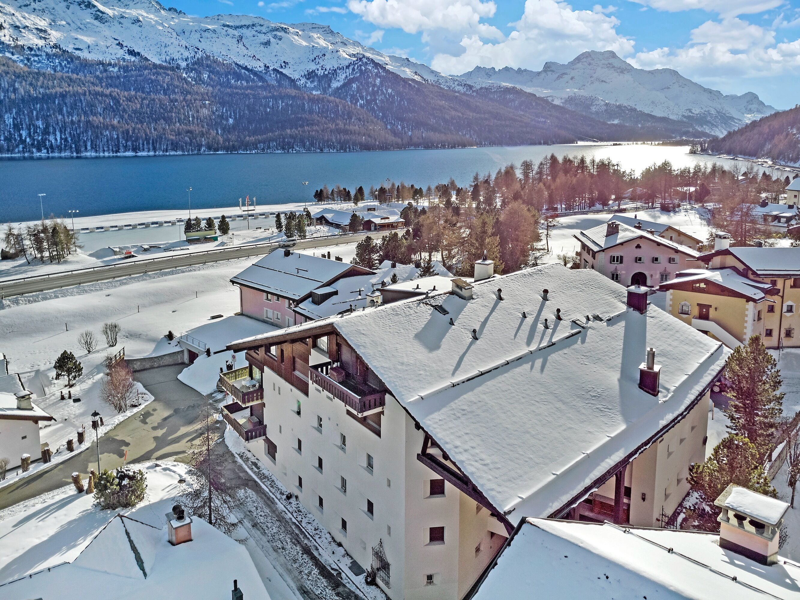 Eine verschneite Stadt mit Gebäuden, einem See und Bergen im Hintergrund.