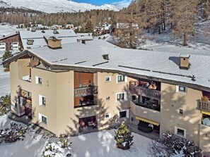 Ein mehrstöckiges Hotel mit Balkonen, einem mit Schnee bedeckten Dach und einer Bergkulisse.