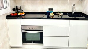 Una cocina moderna con armarios blancos, encimera negra, horno empotrado y fregadero.
