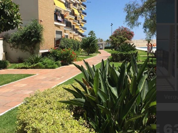 Um edifício residencial com várias varandas, um caminho pavimentado e vegetação bem cuidada.