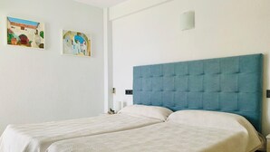 Una habitación de hotel con dos camas individuales, un cabecero azul y dos cuadros enmarcados en la pared.