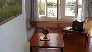 A room with a wooden table, a television on a stand, a bench with striped cushions, and a window with curtains.