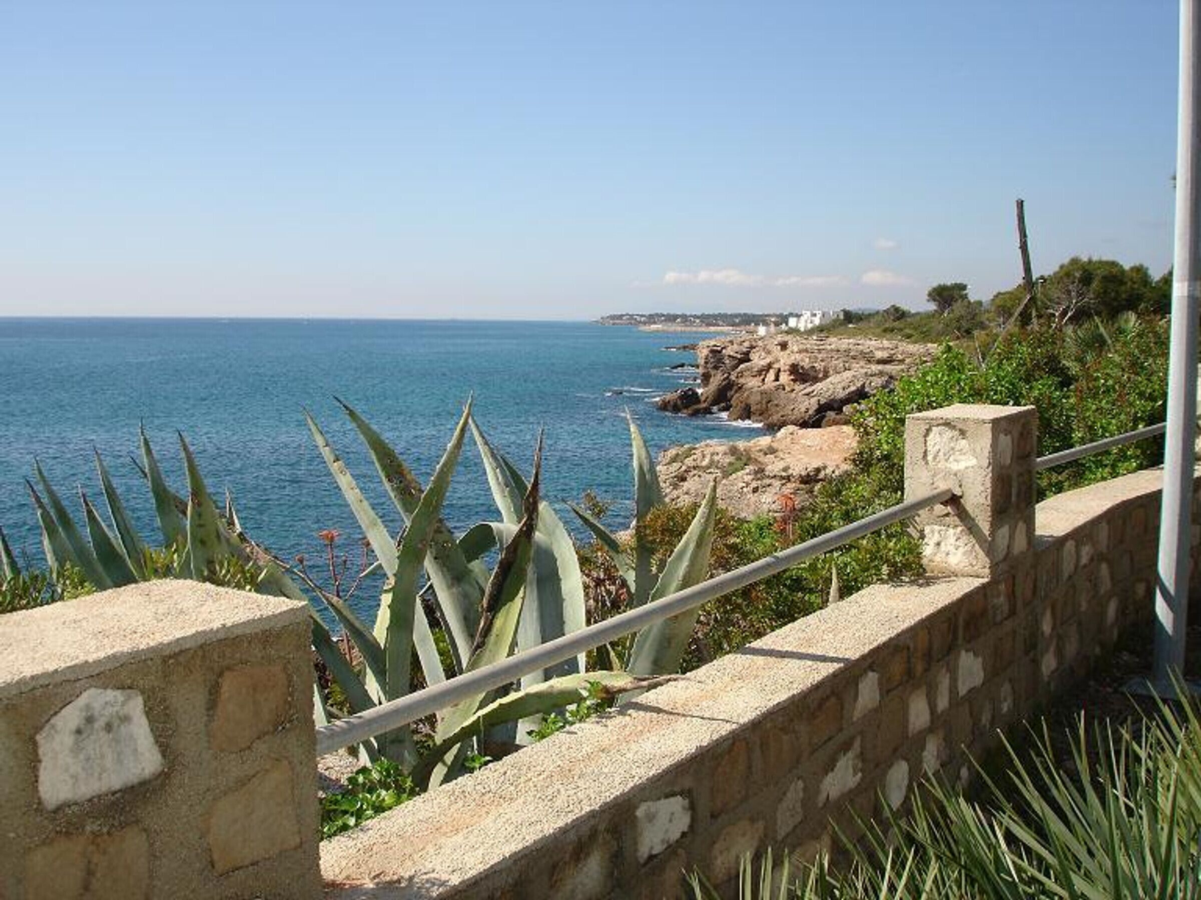 A coastal view with a stone wall and a metal railing overlooking the sea.
