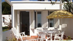 A white building with a patio area featuring a table and chairs, an open door, and a yellow umbrella.