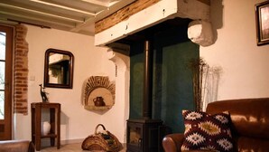 A cozy living room with a fireplace, a leather sofa, a wicker basket, and a rustic brick wall.
