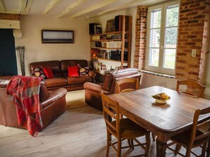 A cozy living room with a brown leather sofa, a wooden dining table, and a bookshelf filled with books. - Charming Cottage Near Vineyards & GR31 Trail - Peaceful Retreat with Modern Amenities (Parassy)