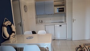 Une cuisine compacte équipée d’un four à micro-ondes, d’un évier et d’un lave-vaisselle. On y trouve une table à manger avec des chaises, ainsi qu’un gilet de sauvetage accroché au mur.