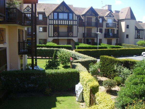 A courtyard with neatly trimmed hedges, a statue, and a row of Tudor-style buildings with balconies. - Appartement à 50 m de la mer (Ouistreham)