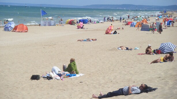 Une plage avec des tentes et des gens qui prennent un bain de soleil.