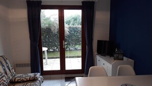 Une pièce comprenant un canapé, une table, un téléviseur et donnant sur l’extérieur grâce à une porte vitrée.