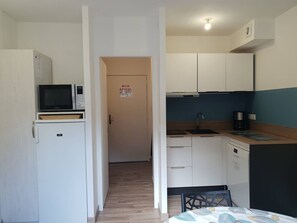 Kompakti keittiö, jossa on valkoiset kaapit, mikroaaltouuni ja kahvinkeitin.