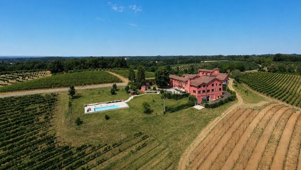 A large estate with a swimming pool, surrounded by expansive vineyards and a prominent red building. - Villa in Piedmont with private pool in beautiful vineyard of Tenuta CostaRossa (Piemonte)