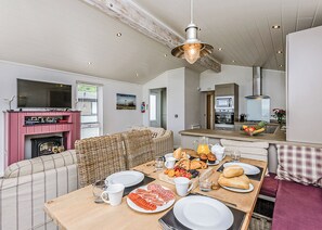 A cozy living room with a fireplace, a dining area with breakfast, and a kitchen with modern appliances. - Osborne Premier Lodge (Wootton, Nr Cowes)