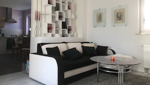 Ein modernes Wohnzimmer mit einem schwarz-weißen Sofa, einem Glastisch und einer weißen Regaleinheit an der Wand.