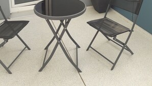 Ein kleiner Sitzbereich im Freien mit einem runden Tisch, zwei Stühlen, einer Schiebetür und einem Blumentopf.
