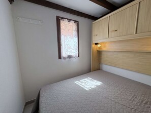 Una habitación pequeña con una cama individual, una ventana con cortina, cabecero de madera y una lámpara.