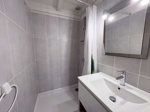 A modern bathroom with grey tiles, a white sink, a mirror, and a shower with a white curtain.