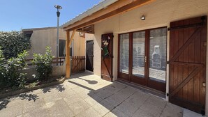 Un edificio con un porche cubierto, puertas de madera y un pequeño jardín.