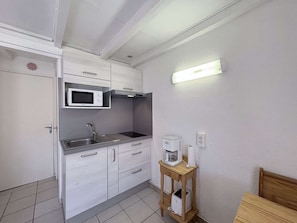 A compact kitchen with white cabinetry, a microwave, a sink, a coffee maker, and a wooden side table.