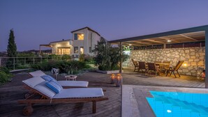 A modern outdoor pool area with lounge chairs and a stone wall. - Luxury Villa Hara with private pool (Malevizi)