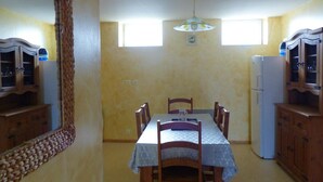 Een kleine keuken met een eettafel, stoelen, een koelkast en houten kastjes.