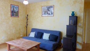 Een woonkamer met een blauwe bank, een houten salontafel en een boekenkast.