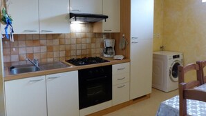 Een kleine keuken met een gasfornuis, oven en koffiezetapparaat. Er staat een wasmachine in de hoek.