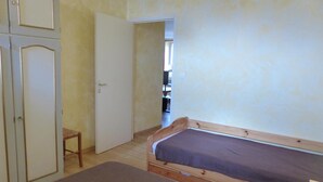 Een slaapkamer met een houten bed, een klein houten krukje en een witte deur.
