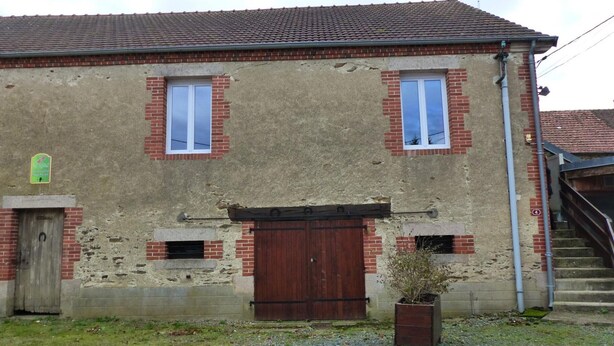Een gebouw met twee verdiepingen, voorzien van een rode dakbedekking, een houten deur en twee ramen met witte kaders.