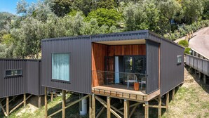 A modern, elevated wooden structure with a balcony, surrounded by lush greenery. - Hidden Valley Waiheke (Waiheke Island)