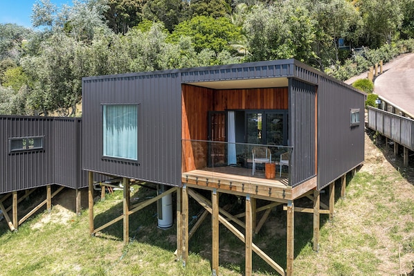 Una estructura de madera moderna y elevada con balcón, rodeada de exuberante follaje.