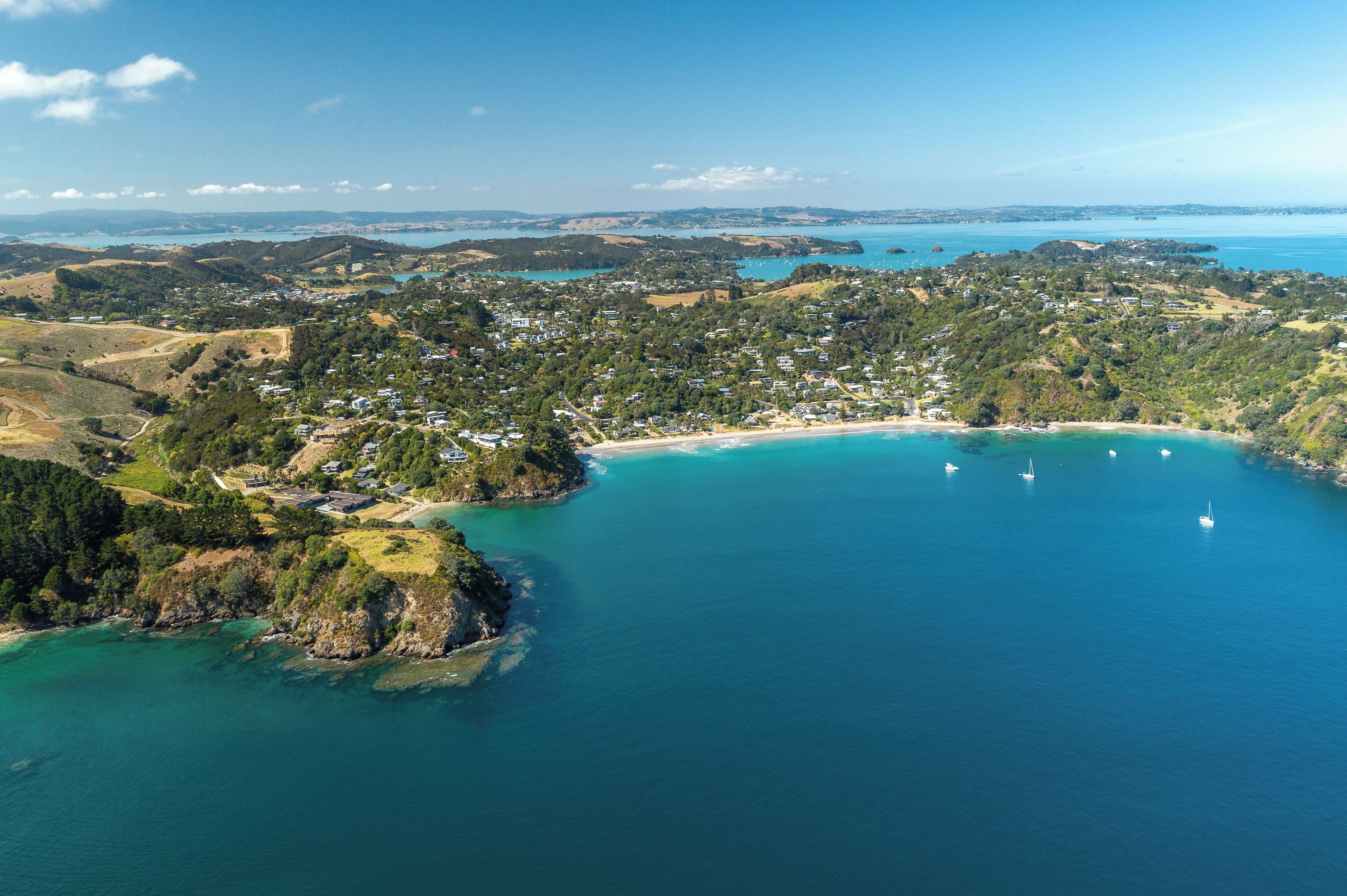 An aerial view of a coastal town with a beach, boats, and lush greenery.
