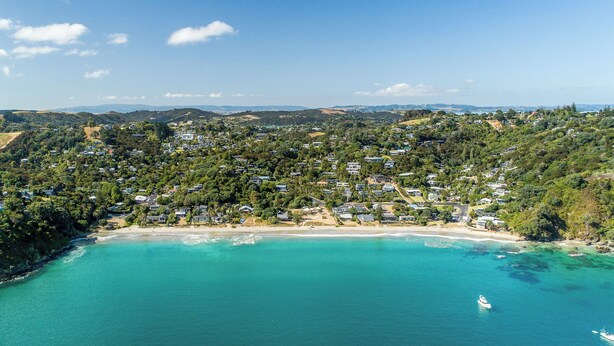An aerial view of a coastal town with a beach, houses, and boats. - Hidden Valley Waiheke (Waiheke Island)