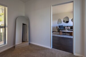 Ein modernes Wohnzimmer mit dunklem Holzboden, einem hellen Teppich, einer Couch mit Kissen, einem Couchtisch und zwei an der Wand befestigten Spiegeln.