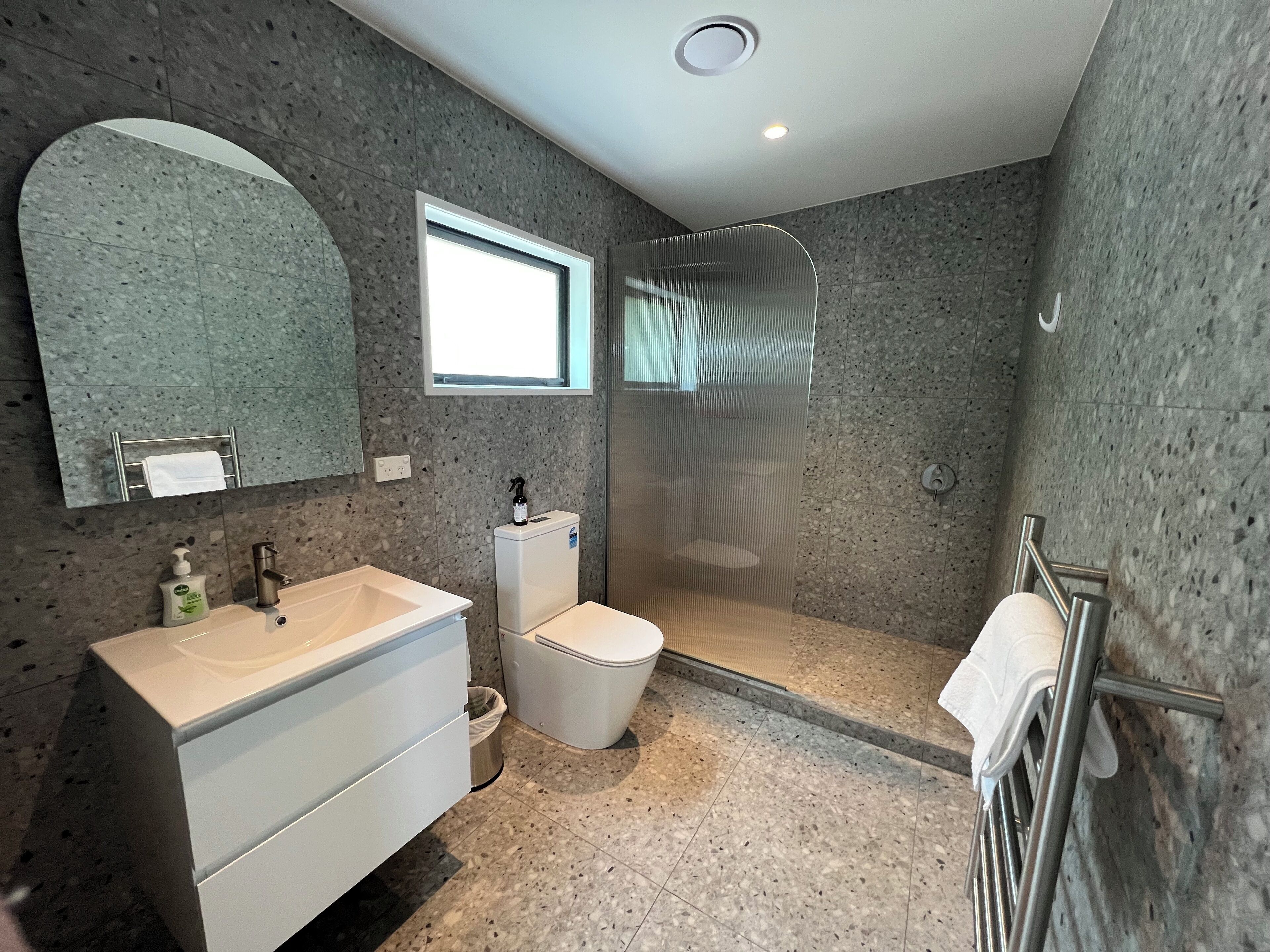 A modern bathroom with a granite countertop sink, a toilet, a shower enclosure, and a large mirror.