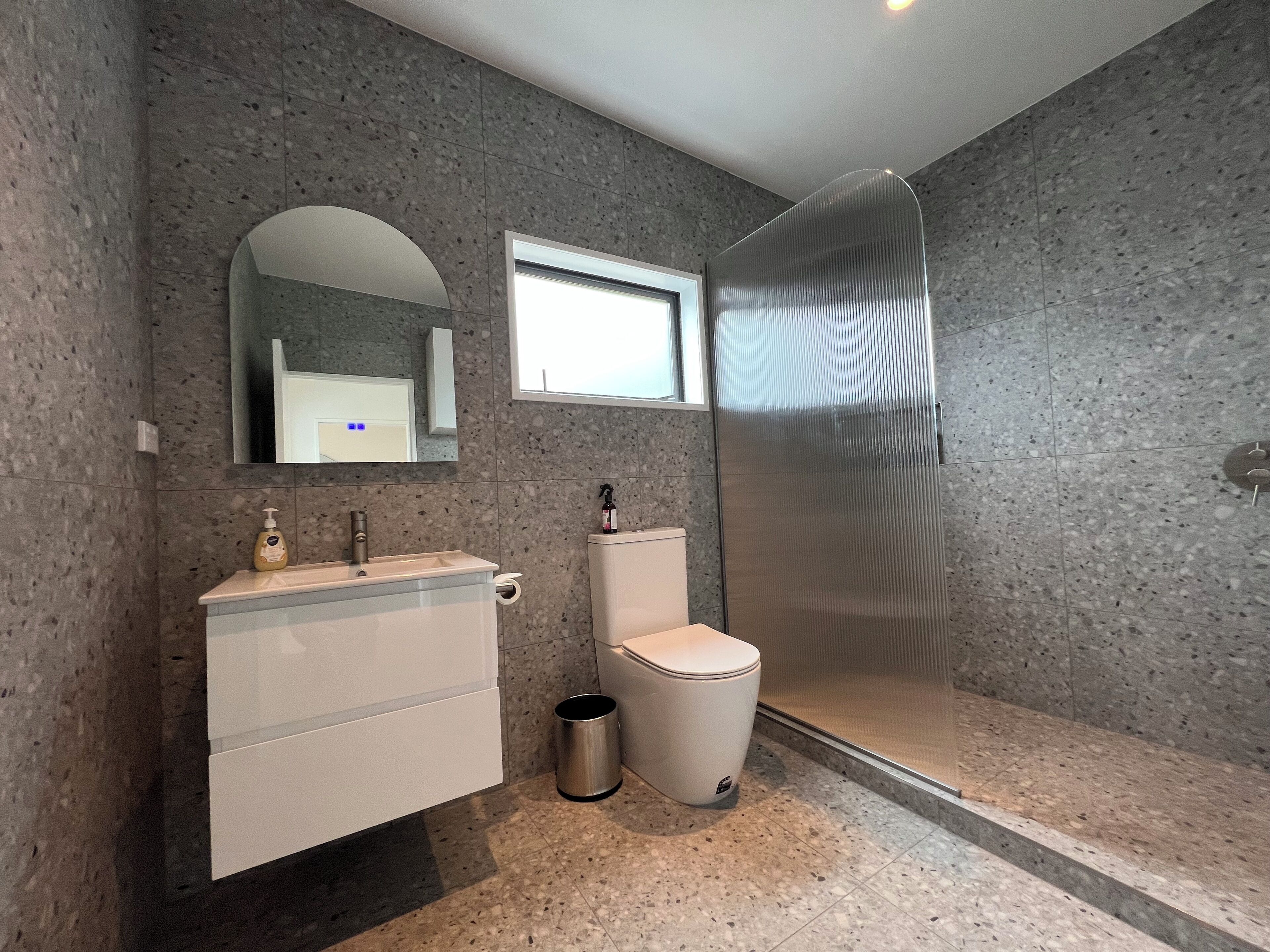 Een moderne badkamer met een granieten aanrecht, toilet, douchecabine en spiegel.