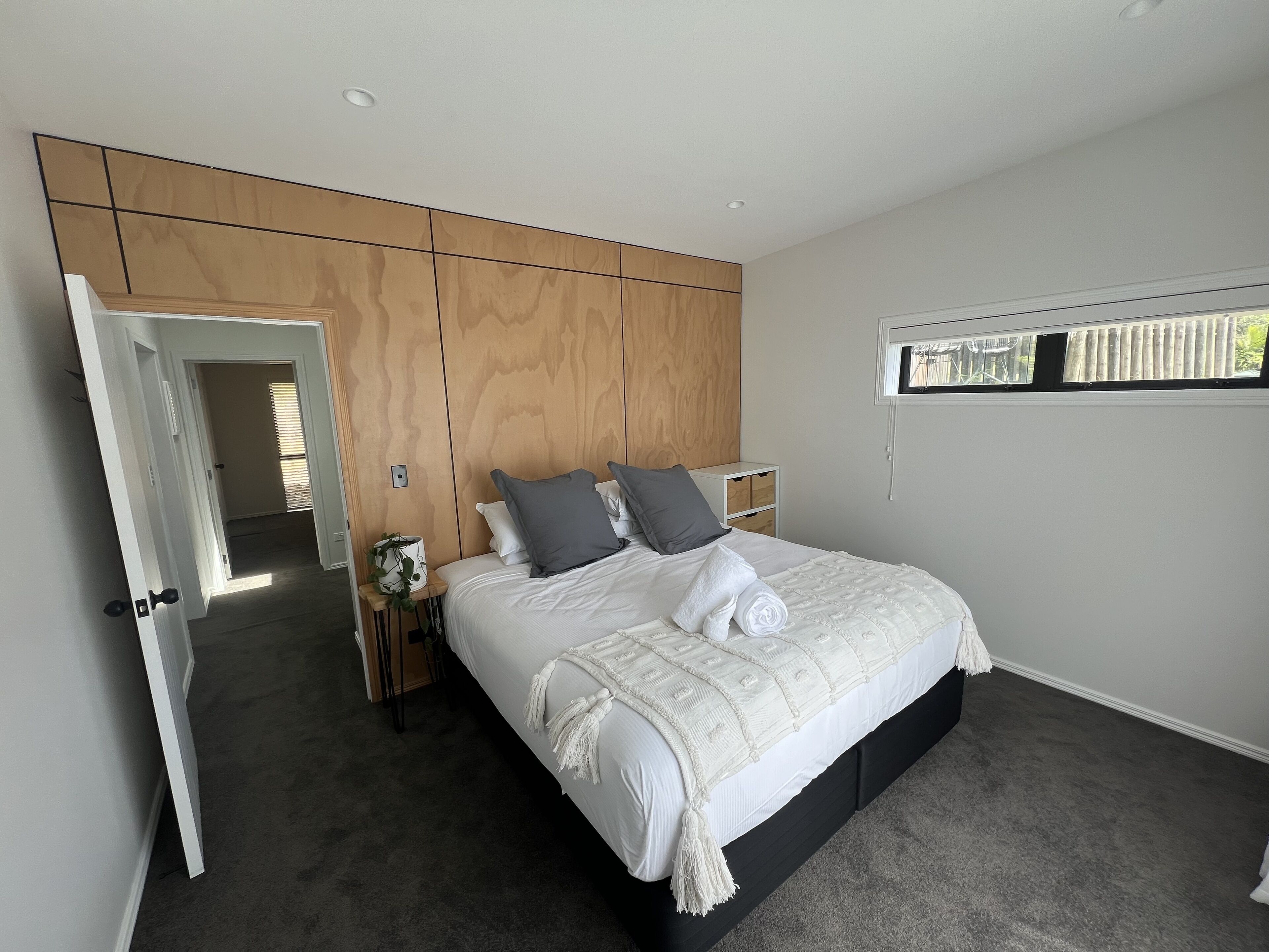 Een slaapkamer met een groot bed, een houten garderobe, een nachtkastje met een plant en een raam met zonwering.