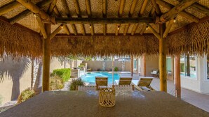 A covered outdoor area with a pool, lounge chairs, and a table with a woven centerpiece.
