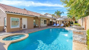 A swimming pool with a curved edge, a covered patio area with lounge chairs, and a thatched-roof structure.