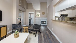 A modern kitchen with white cabinets, a microwave, and a built-in oven. There is a dining area with a table and chairs, and a fireplace in the background.