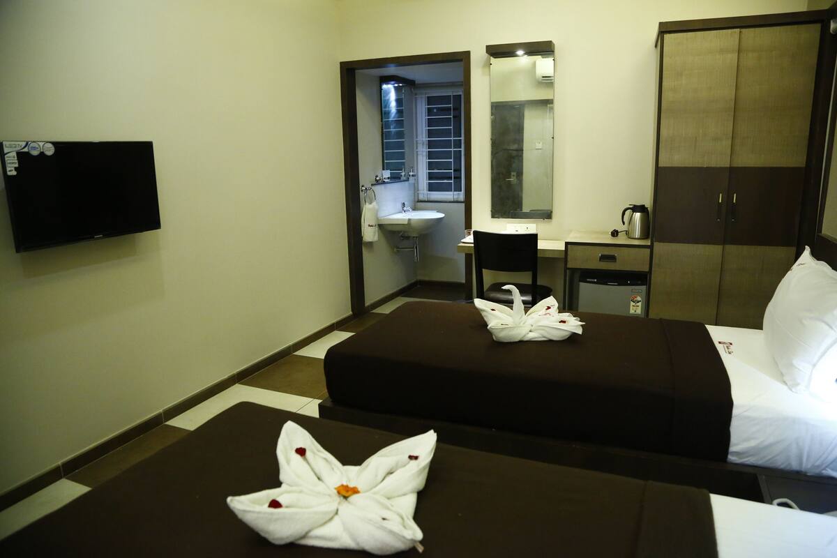 A hotel room with two beds, a TV, a sink, a mirror, a wardrobe, and a coffee maker.