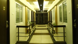 Pasillo de hotel con piso a cuadros, puertas de madera y una barandilla central.