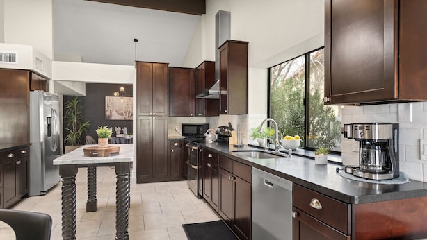 A modern kitchen with dark wood cabinets, stainless steel appliances, and a large window providing natural light. - Perfectly Located Spacious Home with Heated Pool (Scottsdale)