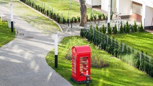 Un camino que lleva a un edificio moderno, con una cabina telefónica roja y bancos.