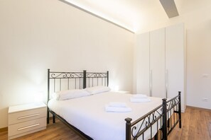 Un lit bien fait, avec du linge de lit et des serviettes blanches, une table de chevet avec des tiroirs et une armoire en arrière-plan.