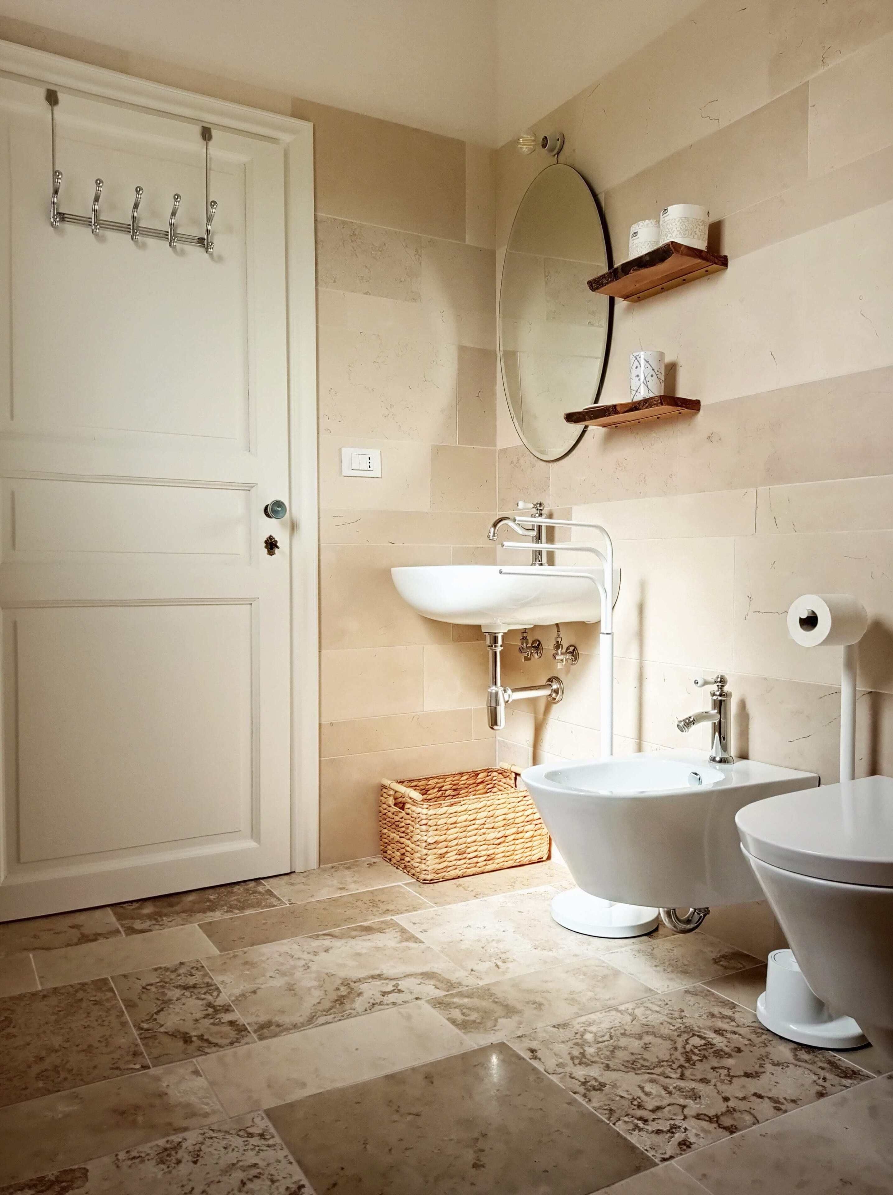 A bathroom with a white door, a white sink, a bidet, and a toilet. There is a mirror on the wall and a shelf with cups.