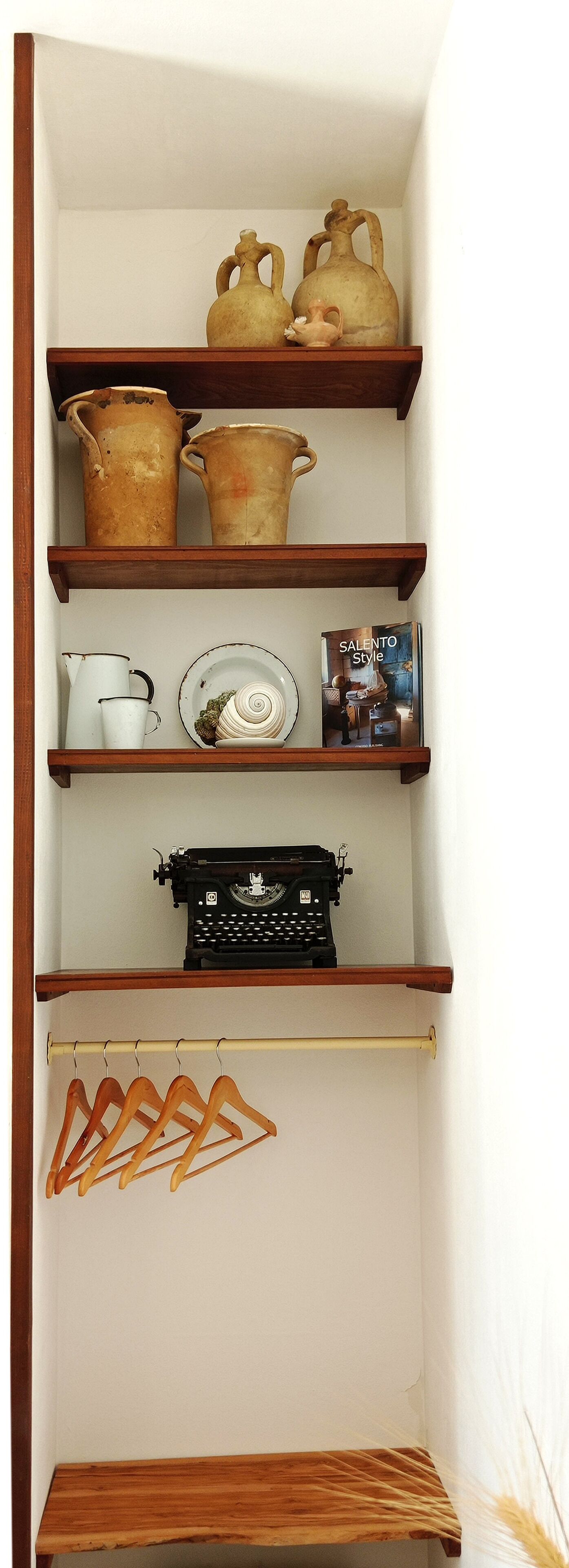 Una estantería de madera con varios utensilios de cocina, incluyendo ollas, una máquina de escribir y un libro titulado 'Salento Style'.
