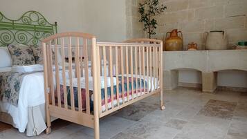 A wooden crib with a colorful quilt, a green metal headboard, a tiled floor, and a stone wall.