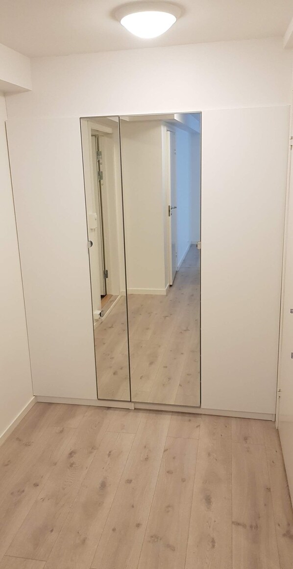 Una habitación con un espejo grande, suelo de madera y paredes blancas.